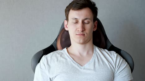 young man is sitting on the armchair with electric massage pillow