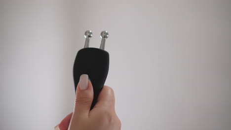 female holds microcurrent facial device in hand. lady checks condition of special device with microcurrent for facial skin treatment after shower