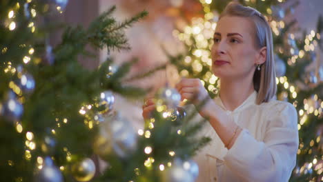 smiling woman placing decorations on christmas tree