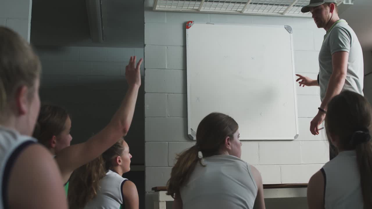 하키 코치 가 로커  ⁇  에서 여자 선수 들 과 함께 게임 계획 을 설명 하고 있다