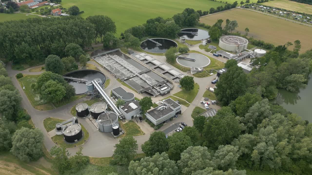High-angle drone view of a wastewater treatment facility surrounded by greenery and farmland.