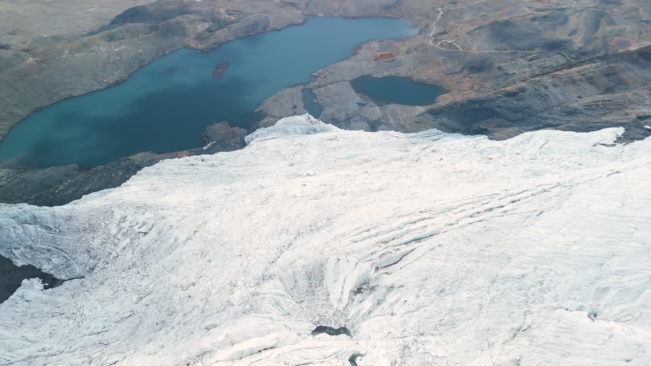 A spectacular high-angle aerial parallax shot sweeps over the vast Pastoruri Glacier, revealing its textured ice field and the deep blue glacial lakes formed by its meltwater in the Andes