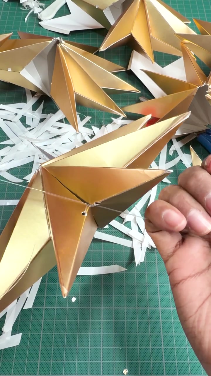 Hands assembling handcrafted metallic Christmas stars in craft workshop, vertical