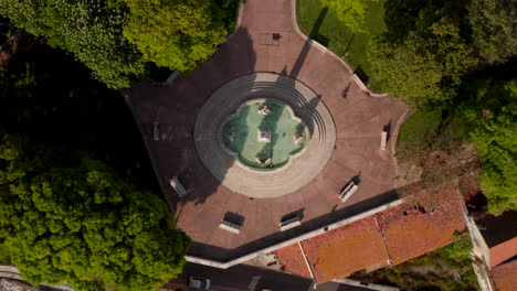 Aerial-birds-eye-overhead-top-down-view-of-city-square-with-park.-Several-benches-around-fountain-in-front-of-Necessidades-Palace.-Zooming-out-footage-from-drone.-Lisbon,-capital-of-Portugal.
