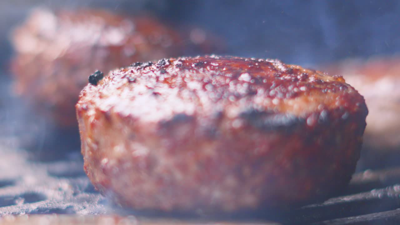 Chef Using Spatula to Flip Large Beef Burger as it Tumbles in Slow Motion and Flames Lick Underside of Patty. Well Done Tasty Delicious Meat Cooked Outside
