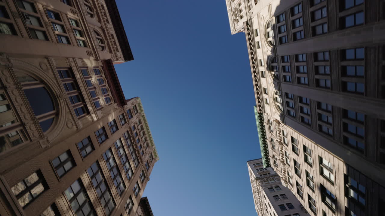 Vista de baixo de edifícios históricos de Manhattan com fachadas ornamentadas sob o céu aberto, arquitetura urbana clássica em Nova York.