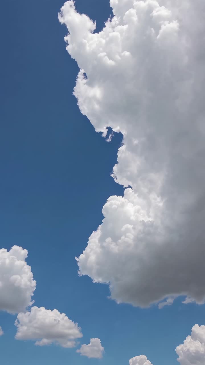 A video captures fluffy white clouds against a vibrant blue sky from a low-angle perspective