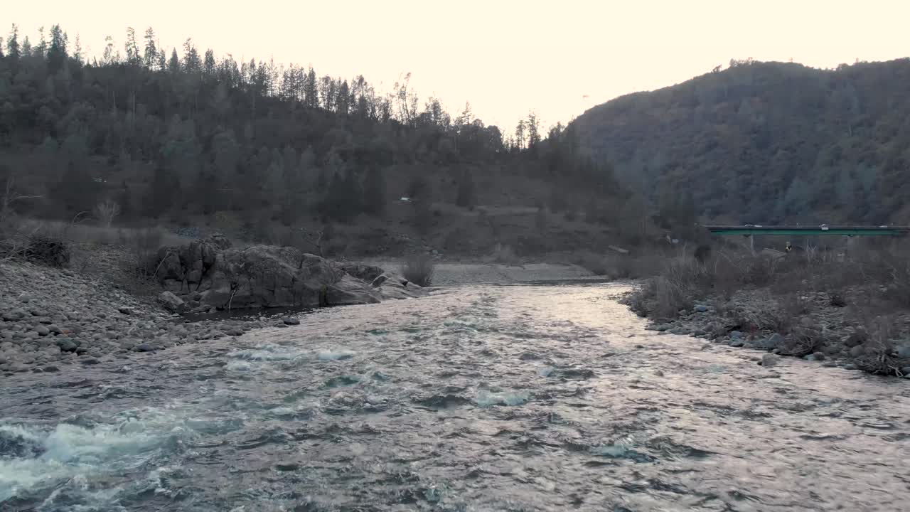 캘리포니아 주 오번의 아메리칸 강에서 물과 바위 위를 낮게 날아다니는 드론 - 초록색 나무와 산으로 둘러싸여