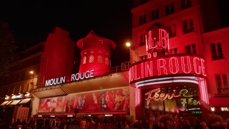 people lining up to enter the moulin rouge in paris - building exterior illuminated nighttime view