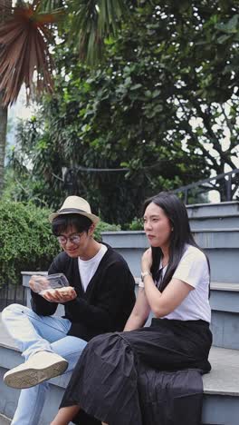 vertical video of romantic asian couple eating street food together while sitting in the park