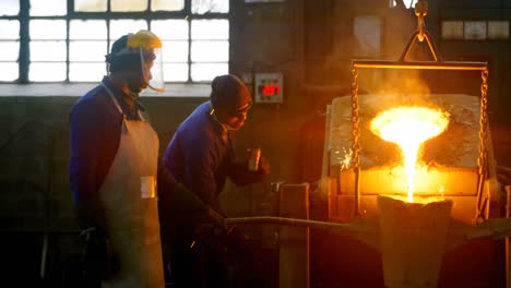 male worker pouring molten metal in mold at workshop 4k