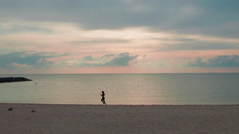 a young woman is captured running along a sandy beach, the ocean waves crashing behind her as she pushes herself to her limits