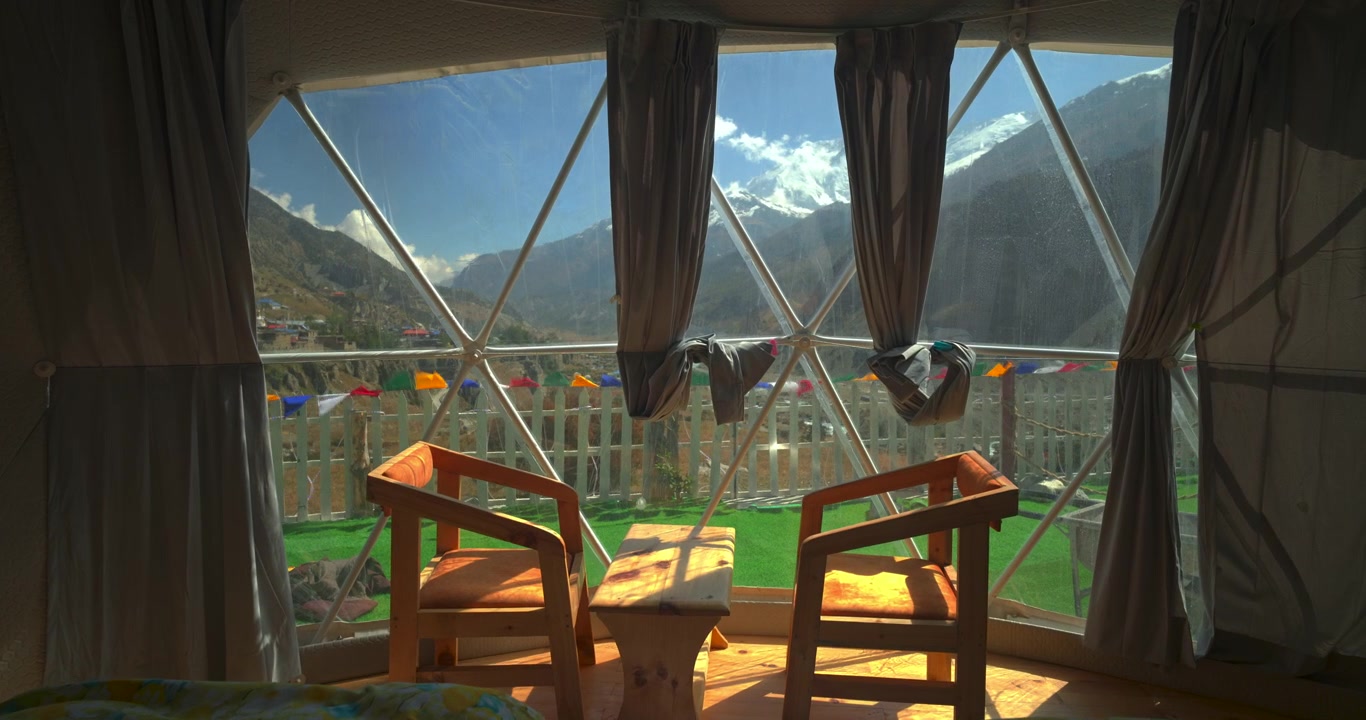 Annapurna Circuit, Manang, Nepal, et luksus glampingtelt med to træstole og et bord, der indrammer panoramaudsigt over sneklædte Annapurna-toppe