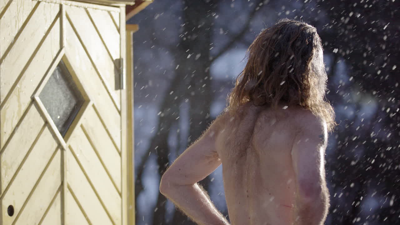 Bare chested wild man turns with huge grin as he enters steaming sauna in snow