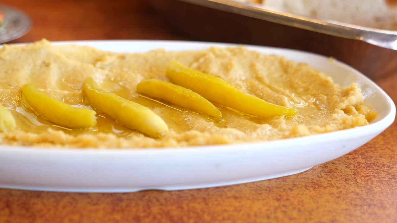 Hummus con peperoni sottaceto e olio d'oliva su un piatto bianco.