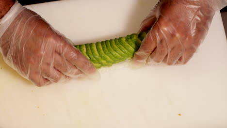 chef uses bamboo mat to set avocado slices on top of rolled sushi rice with shrimp tempura filling - high angle shot