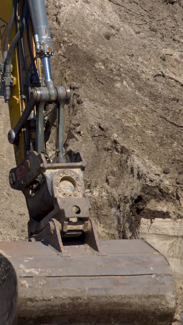 Excavator arm lowers and scoops soil in bright daylight at an active construction site