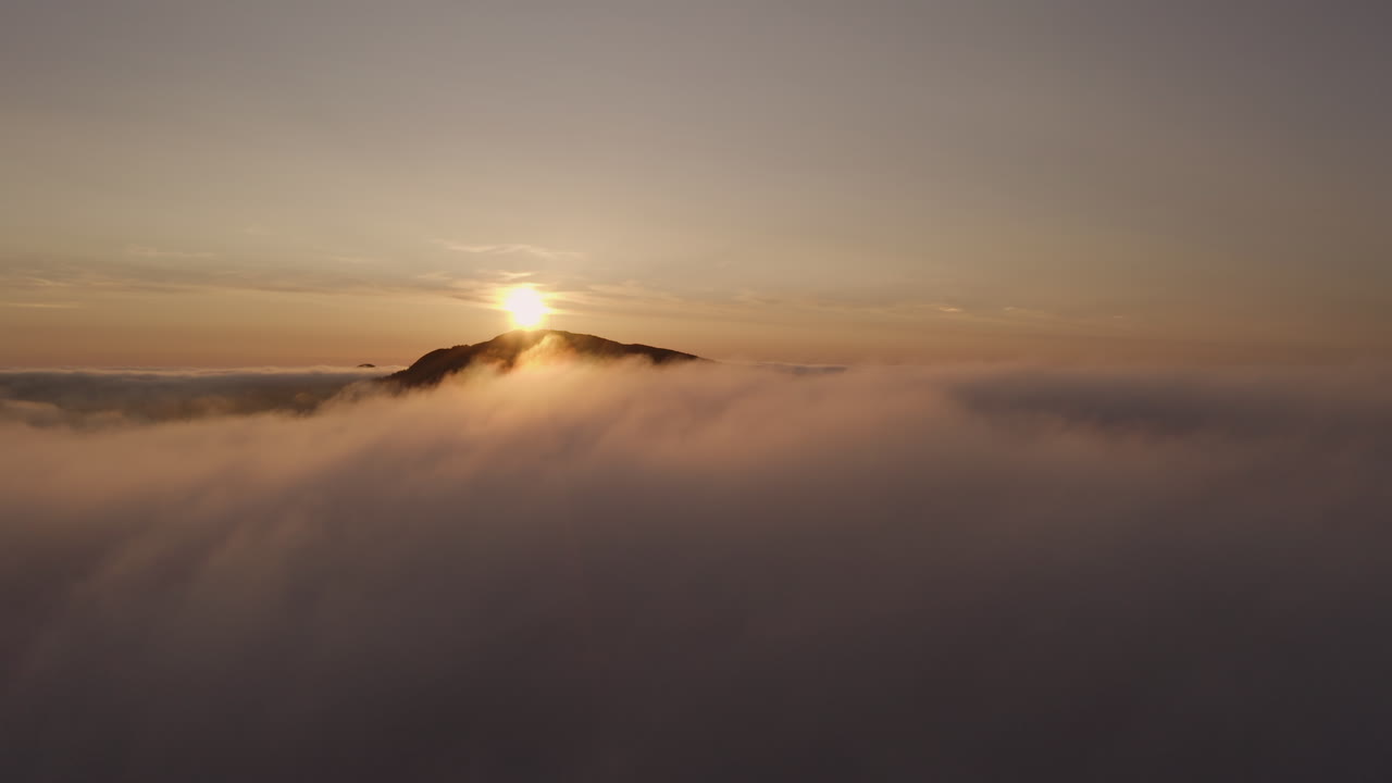 Aerial shot rising up and breaking through the fog to reveal a beautiful sunset