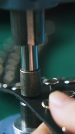 cu: professional designer fixes metal accessories on black leather choker with press machine extreme close view