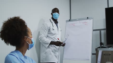 African-american-male-doctor-in-face-mask-giving-presentation-to-mixed-race-female-doctor-in-office