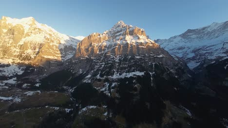 wide aerial view of alpine mountain peaks in golden sunlight and snow fades to deep shadow in valley below