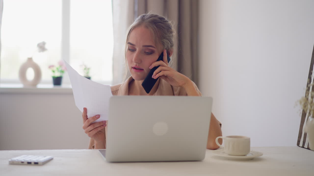 mujer verifica los datos en papel a través del teléfono sentada en la computadora portátil