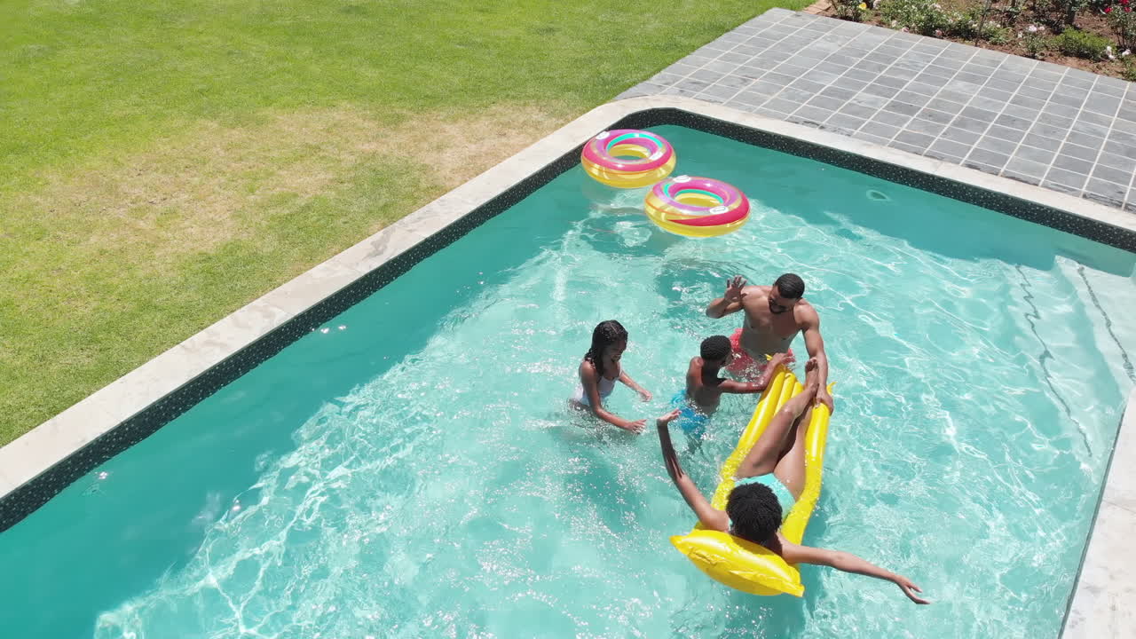 Glade afroamerikanske søn og datter, der hopper i swimmingpoolen til forældrene.