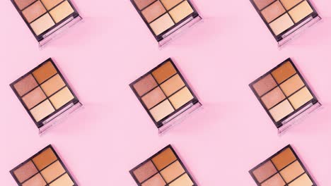 creative make up pattern made of eye shadow palettes rotating on pink background. stop motion