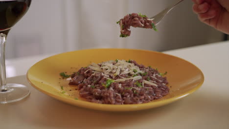 man's hand eating some red wine risotto in a fine dining restaurant, with a glass of wine next to him