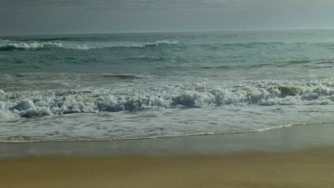 powerful ocean waves roll onto a sandy shore bank, creating white foam as they crash and retreat, shaping the coastline with rhythmic motion.