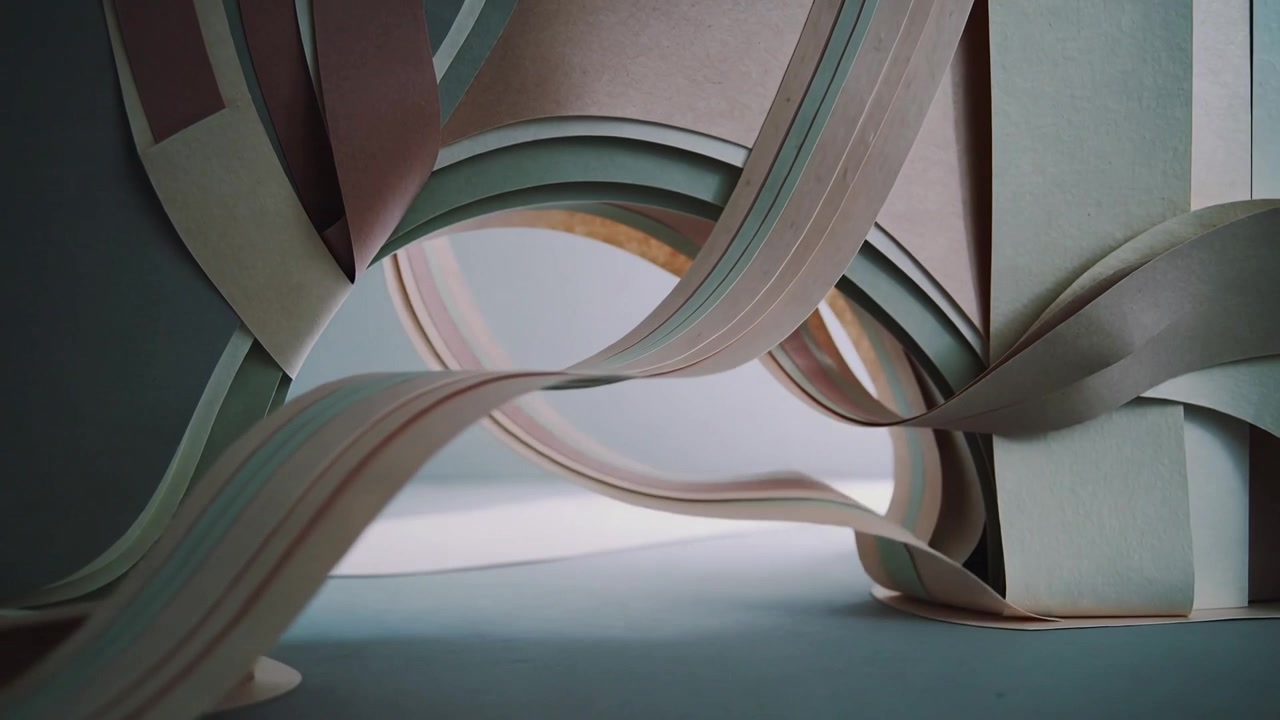 Bandas de papel se movendo, formando laços entrelaçados sobre uma mesa de estúdio, com a sequência avançando em uma coluna empilhada.