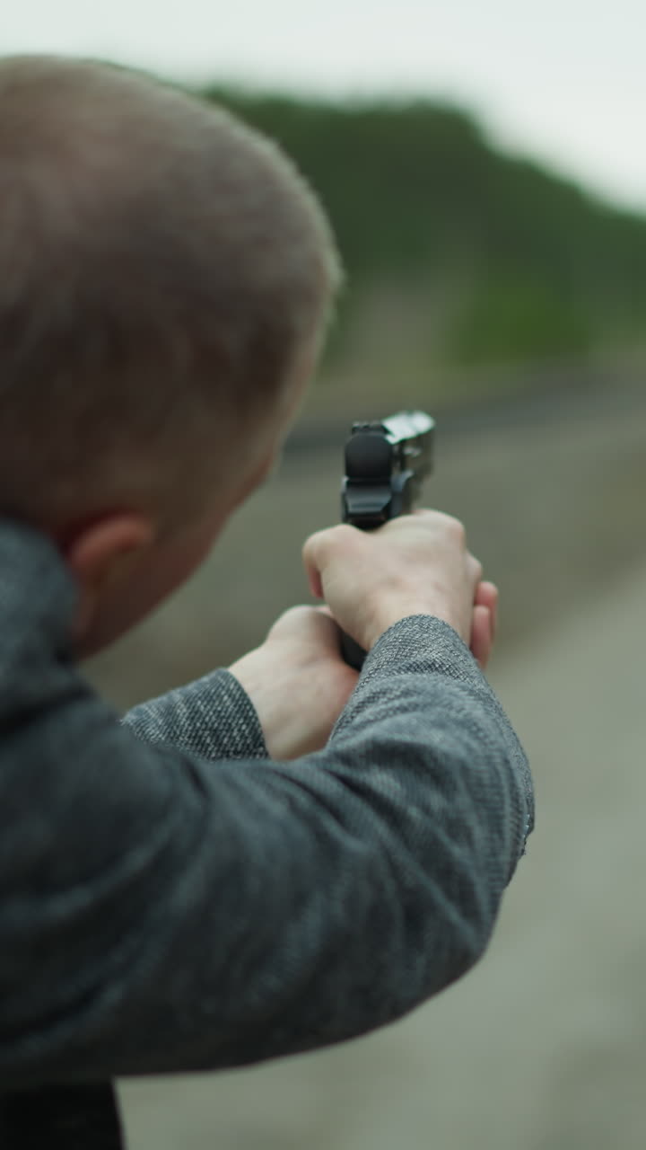 회색 재을 입은 남자가 사막 철도 트랙을 따라 권총을 겨냥하는 뒤에서 근접한 시각