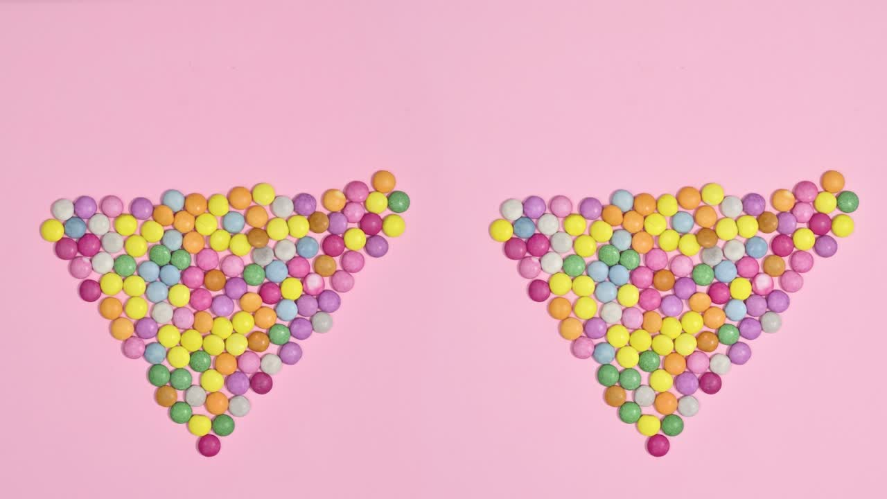caramelos de chocolate de colores que hacen forma de corazón en un fondo rosa brillante. detener el movimiento de colocación plana