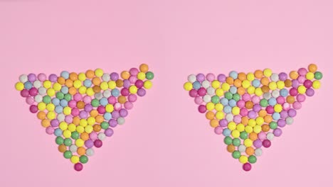 caramelos de chocolate de colores que hacen forma de corazón en un fondo rosa brillante. detener el movimiento de colocación plana