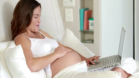 Pregnant-woman-relaxing-on-bed-using-laptop