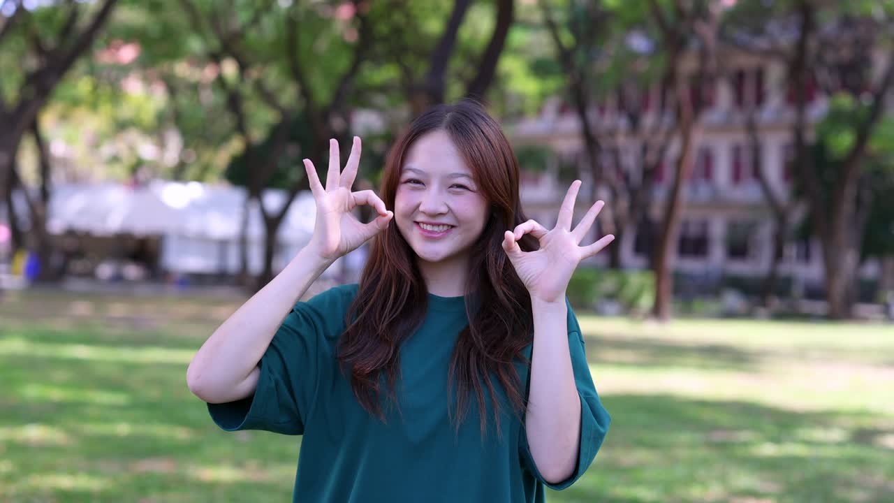 공원에서 미소 지으며 OK 사인을 보내는 젊은 아시아 여성