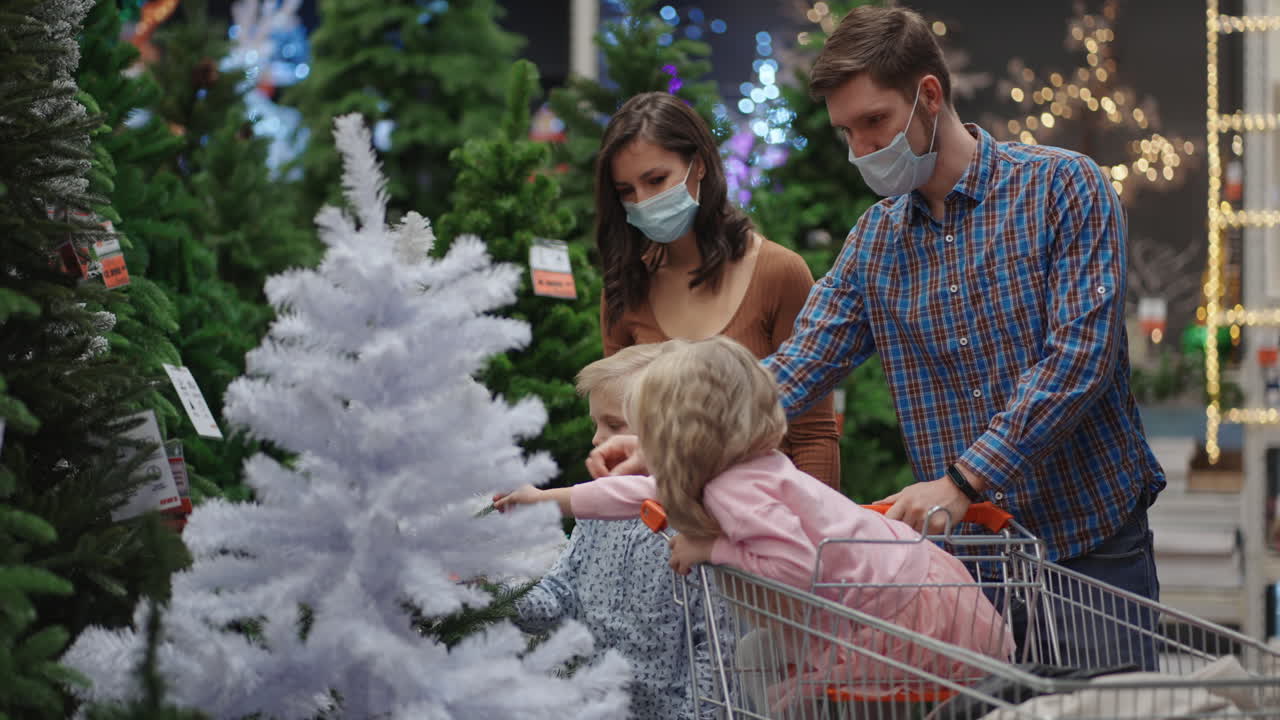 la hija y el hijo de la madre y el padre salen juntos al árbol de navidad. una familia feliz con máscaras médicas en la tienda compra decoraciones y regalos de navidad en cámara lenta