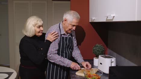 Älteres-Verliebtes-Paar-Beim-Zubereiten-Des-Abendessens.-Ältere-Frau-Umarmt-Ehemann-Von-Hinten-Und-Kocht-Essen-In-Der-Küche