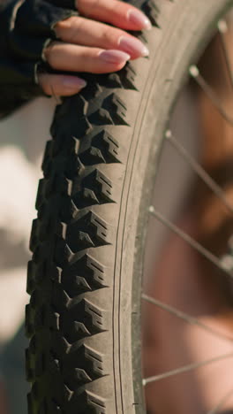 primer plano de un neumático trasero de bicicleta con patrón de banda de rodadura con nudos, inspeccionado por la presión del aire por una persona que lleva guantes negros en un parque soleado, el fondo suavemente borroso
