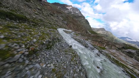 fpv racing drone flying over water stream flowing at fellaria mountain glacier in valmalenco of valtellina, italy