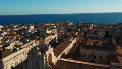 Drone-Volando-Sobre-Syracuse,-Mostrando-Edificios-Históricos-Y-Catedral,-Culminando-En-Un-Impresionante-Horizonte-Costero-Con-Mar