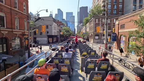 first-person view of toronto king street from moving hop-on hop-off sightseeing bus, with tourists seated enjoying tour among towering skyscrapers and bustling car traffic, canada