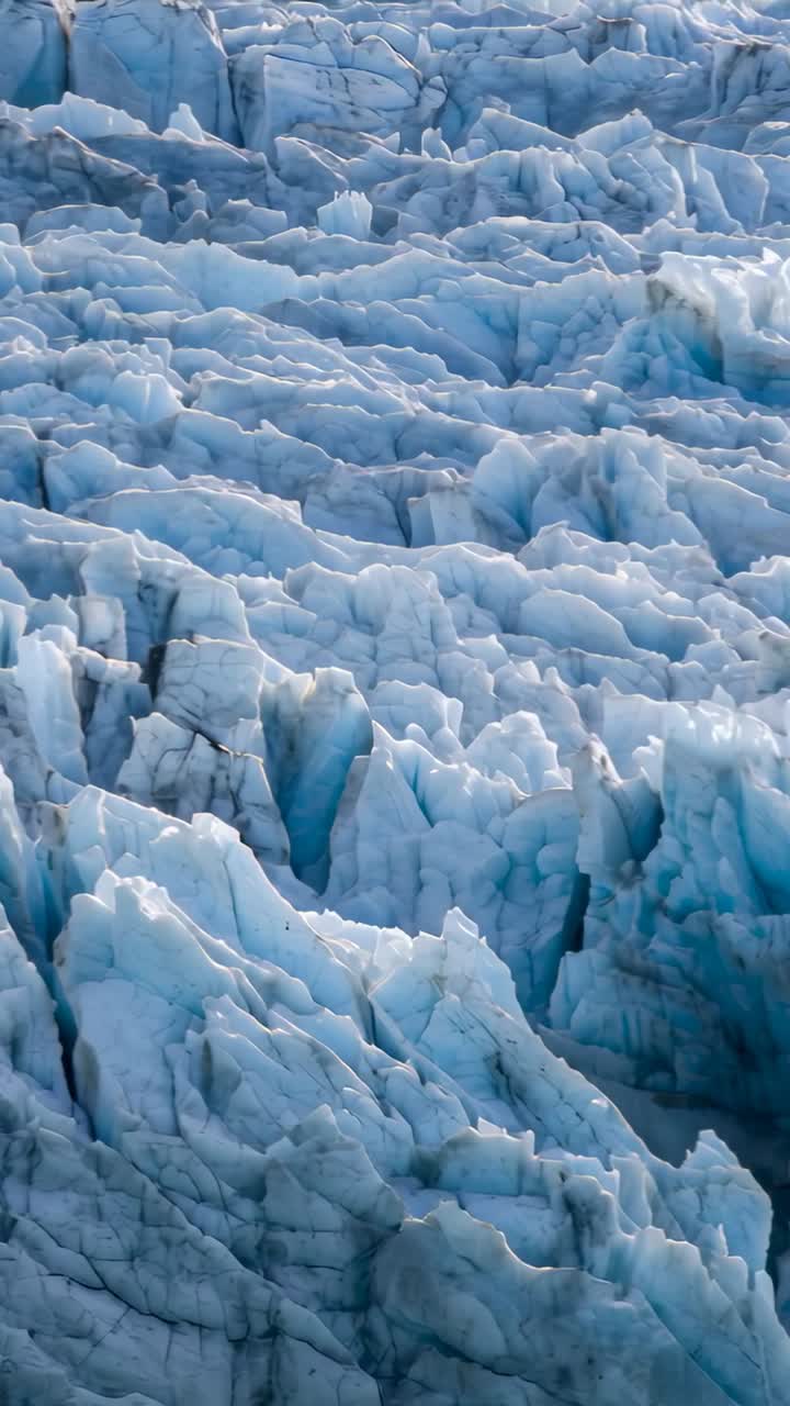 Video verticale: drone che effettua una panoramica, rivelando la superficie del ghiacciaio dalla scogliera per mostrare crepacci e seracchi