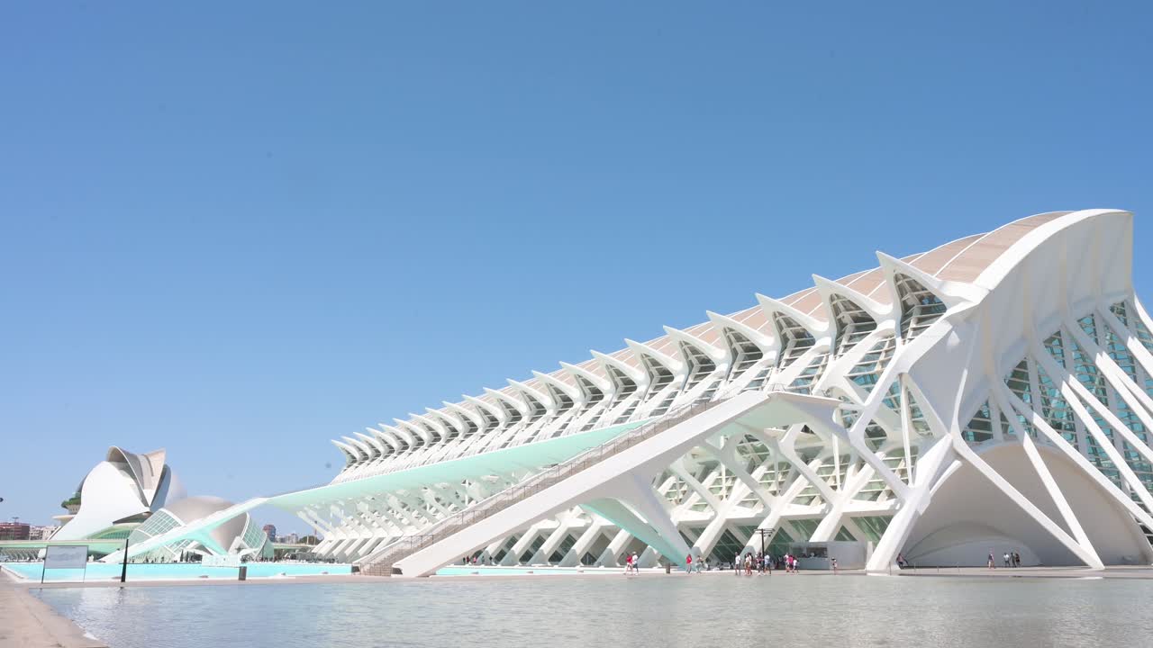 A tilt-down shot captures visitors strolling across the frame in front of the Science Museum, located within Valencia's City of Arts and Sciences complex, the city’s leading tourist destination.