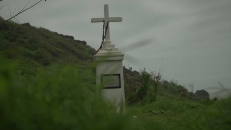 white ancient tombstone in shape of a cross in a forest near the beach under grey sky