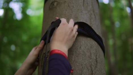 un primer plano de una joven que está tratando de atar una hamaca con un árbol