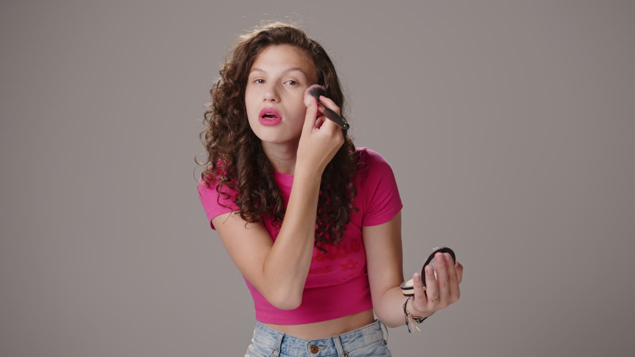 sonriente joven atractiva morena con camisa rosa aplica maquillaje con pincel