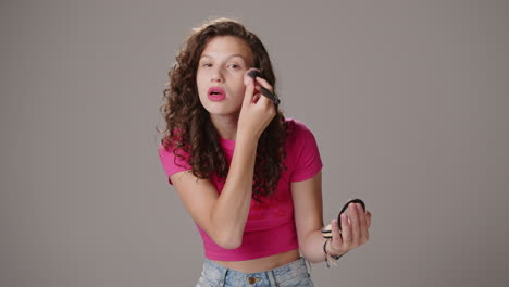 smiling young attractive brunette with pink shirt applies makeup with brush