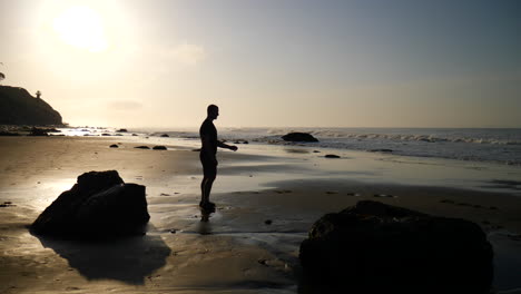 A-man-and-his-pet-dog-companion-running-around-and-playing-together-on-the-beach-at-sunrise-in-Santa-Barbara,-California-SLOW-MOTION