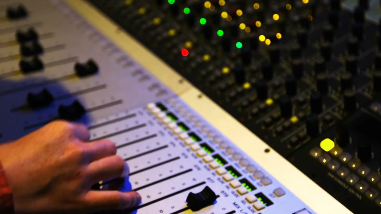 Reacting to onscreen FOCUS label, tech's right-hand in red plaid adjusting fader at studio to mix